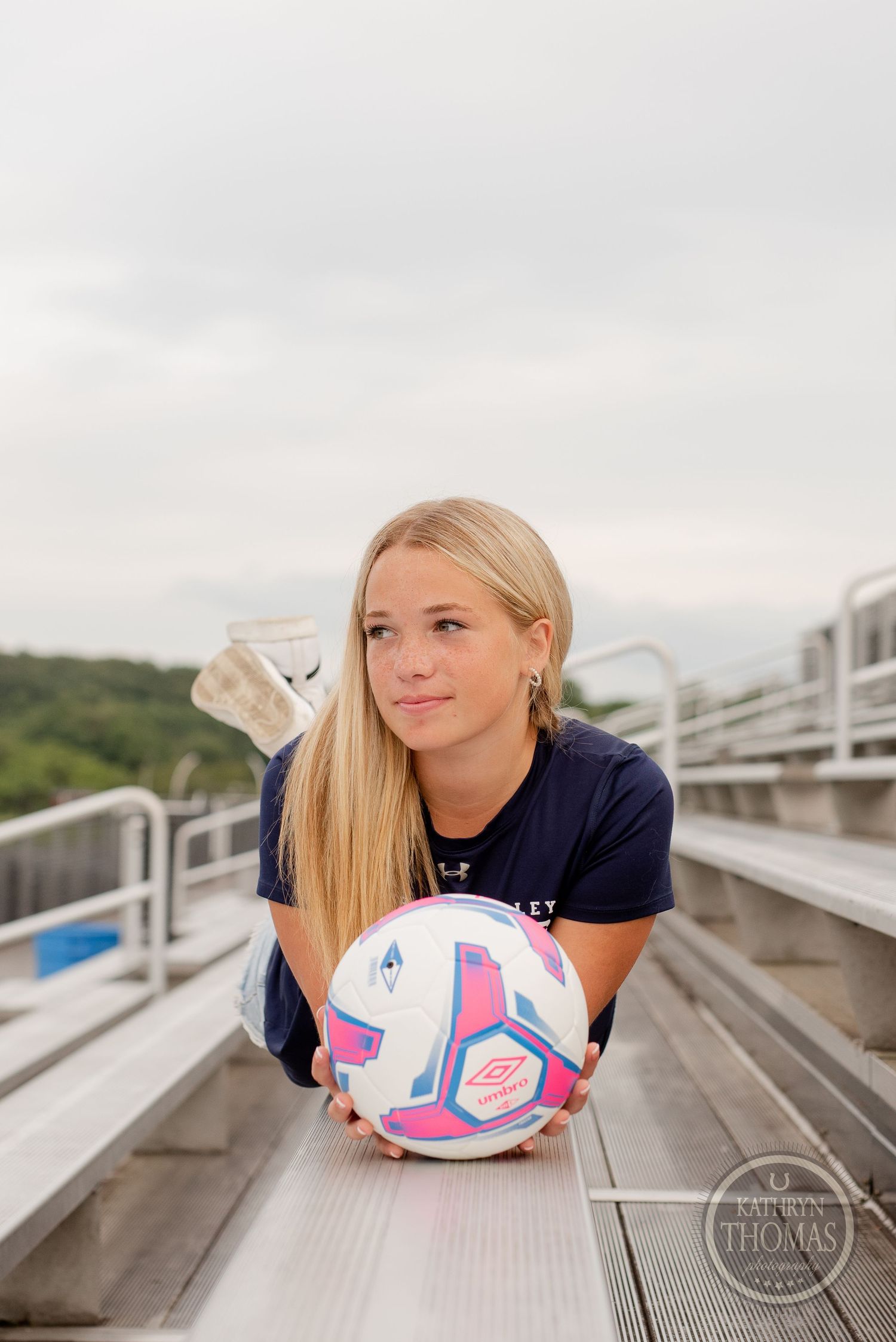 Soccer player laying on metal bleachers with ball during outdoor sports portrait session.