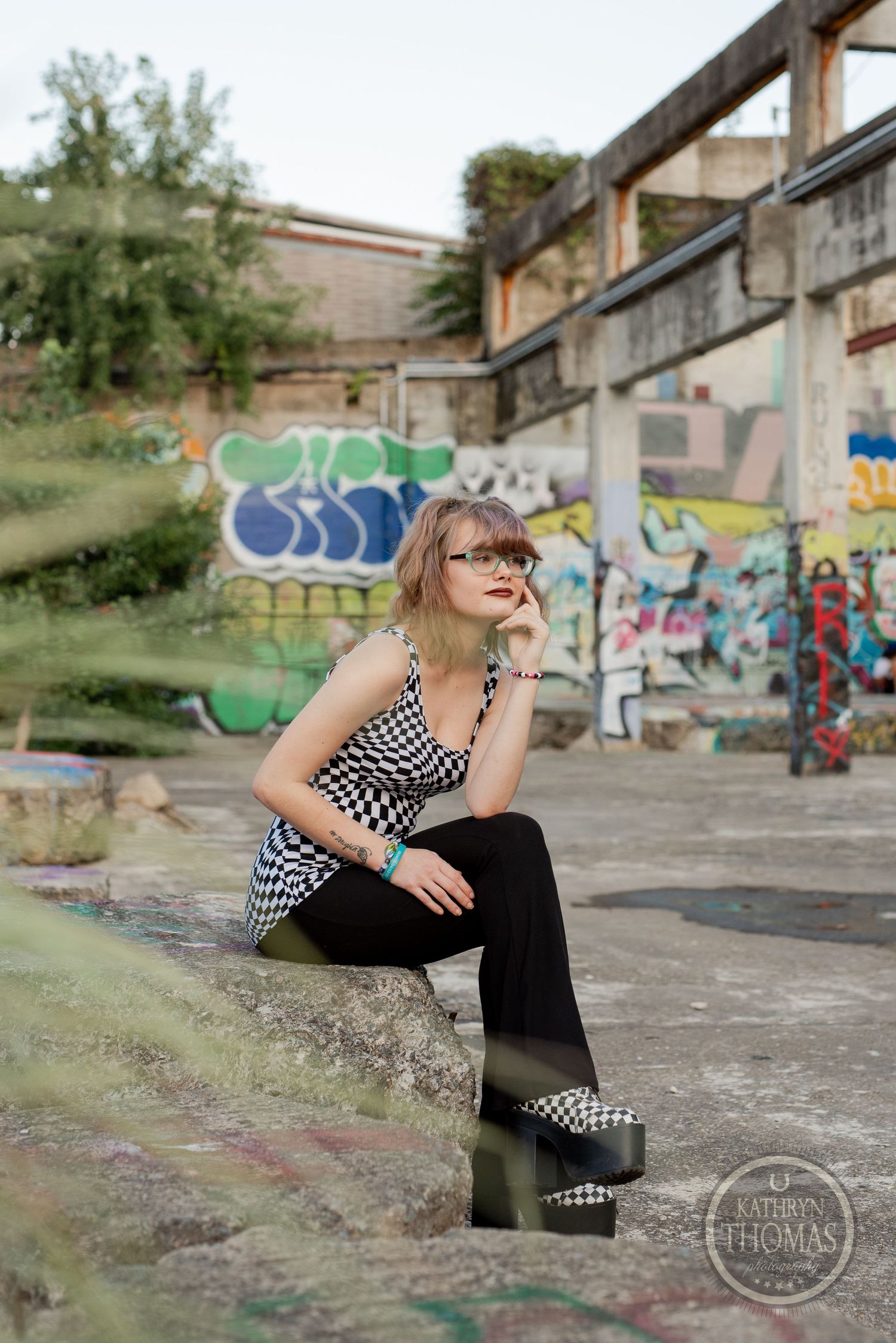 Artistic portrait against graffiti-covered concrete structure with natural lighting and urban elements.