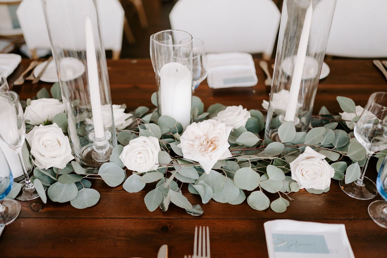 Wedding reception table decorated with white candles, eucalyptus garland and roses.
