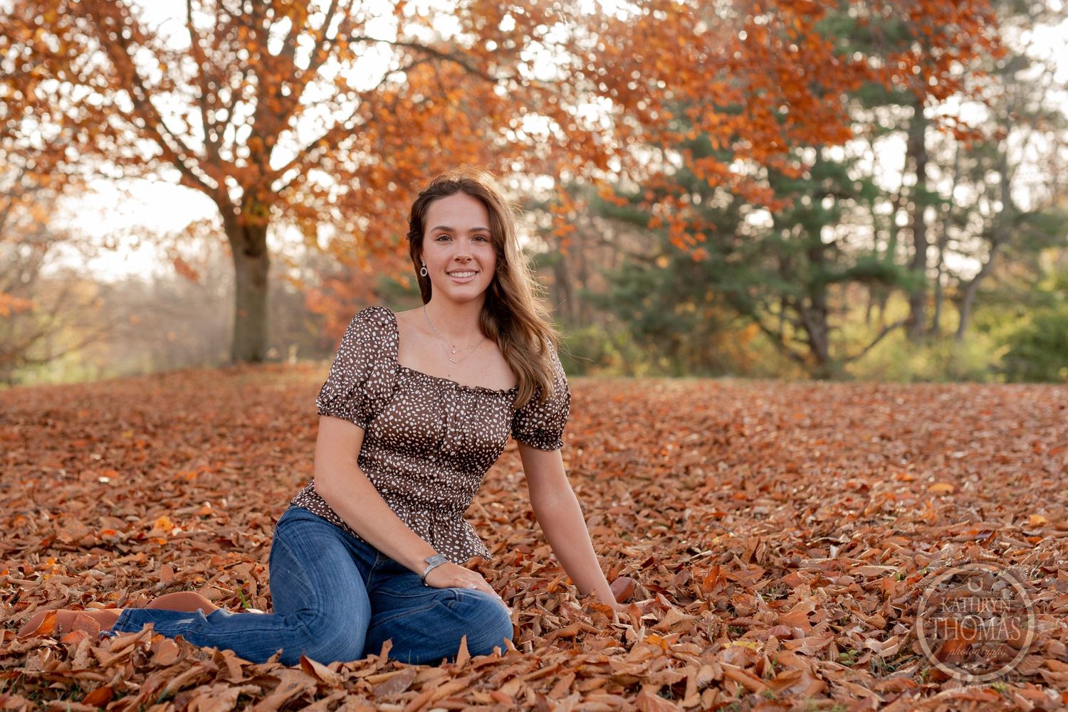 Casual outdoor portrait session surrounded by fallen autumn leaves on ground.