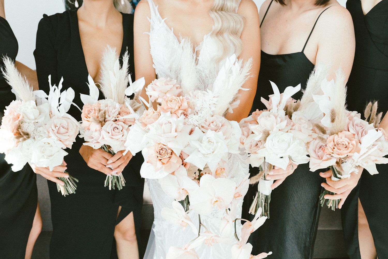 Close up of pink and white wedding bouquets held against black bridesmaid dresses.
