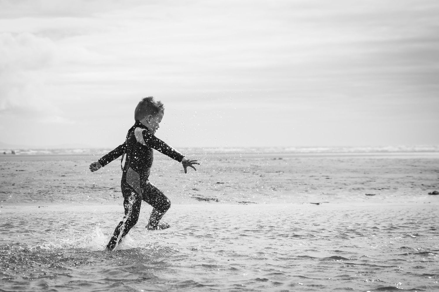 Silhouette jumping in shallow water at the beach in black and white.
