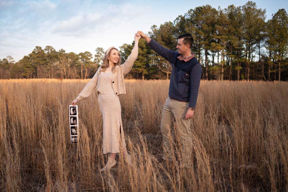 A couple celebrates in a tall grass field during their pregnancy announcement photoshoot.