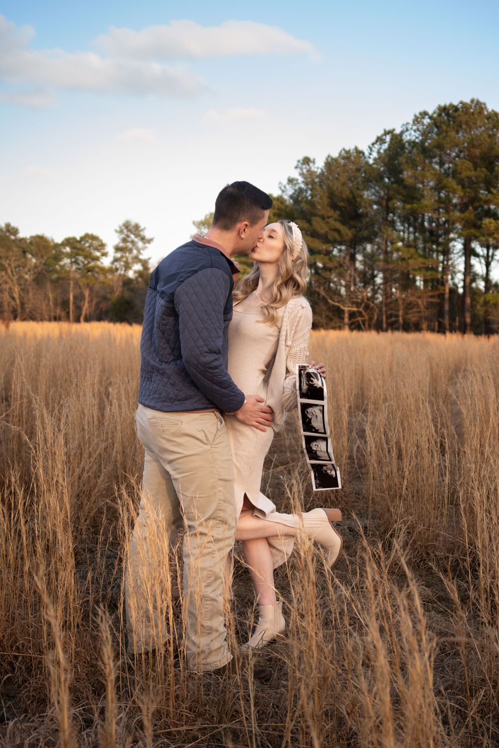 A couple poses romantically in a golden field during sunset for their pregnancy announcement photos.