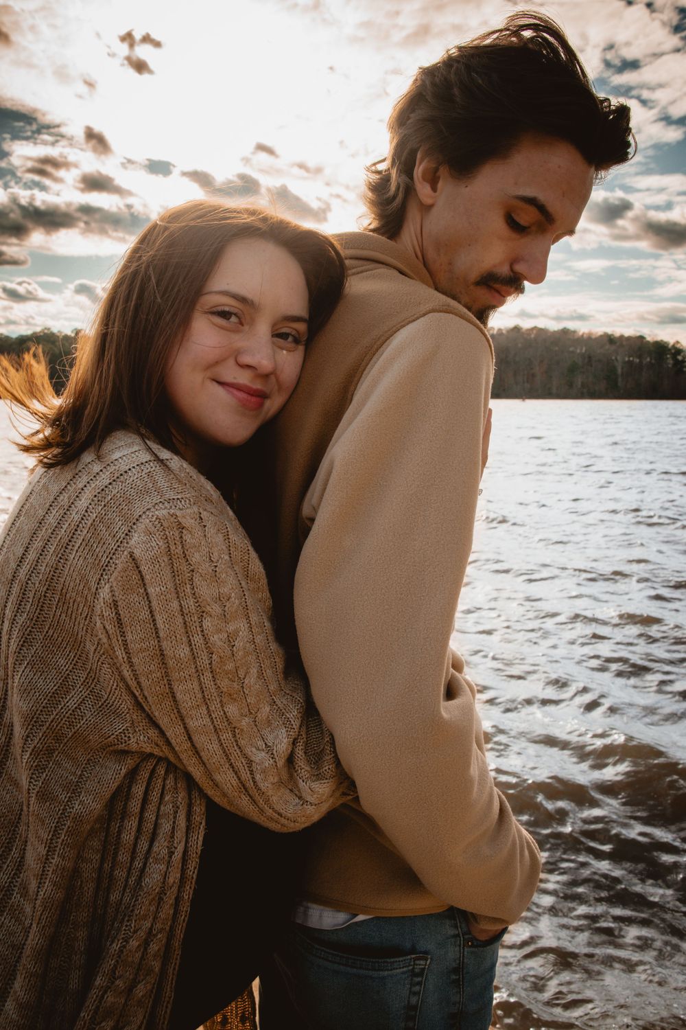 A couple shares an intimate embrace by a lake during golden hour.