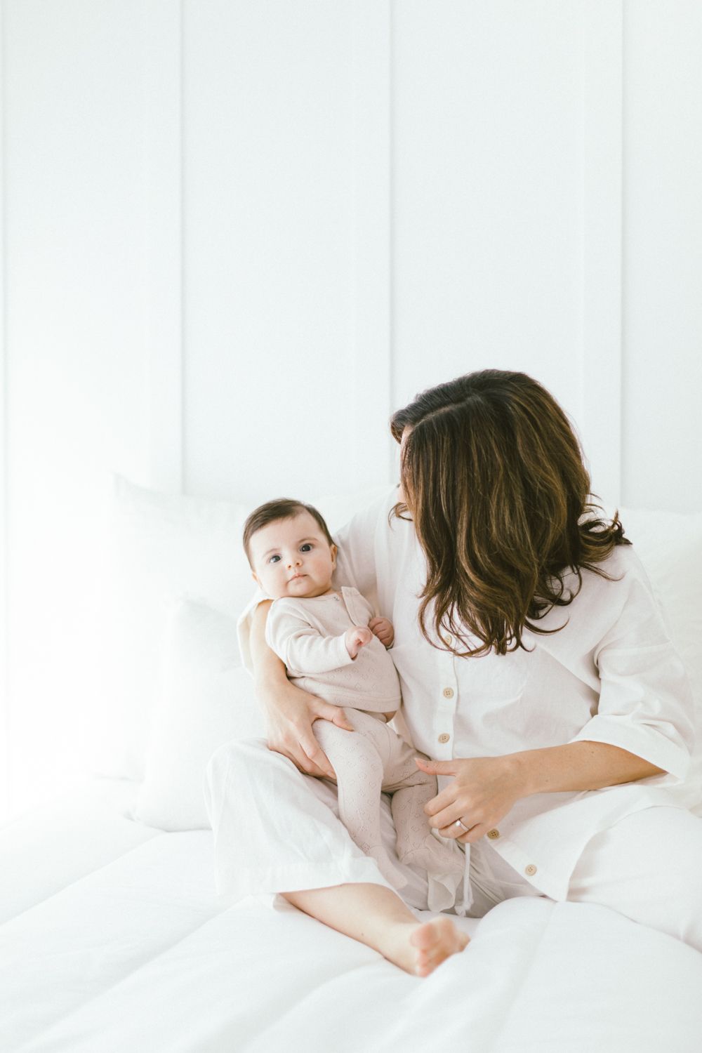 Tender moment between parent and baby on white bedding in bright minimalist setting.