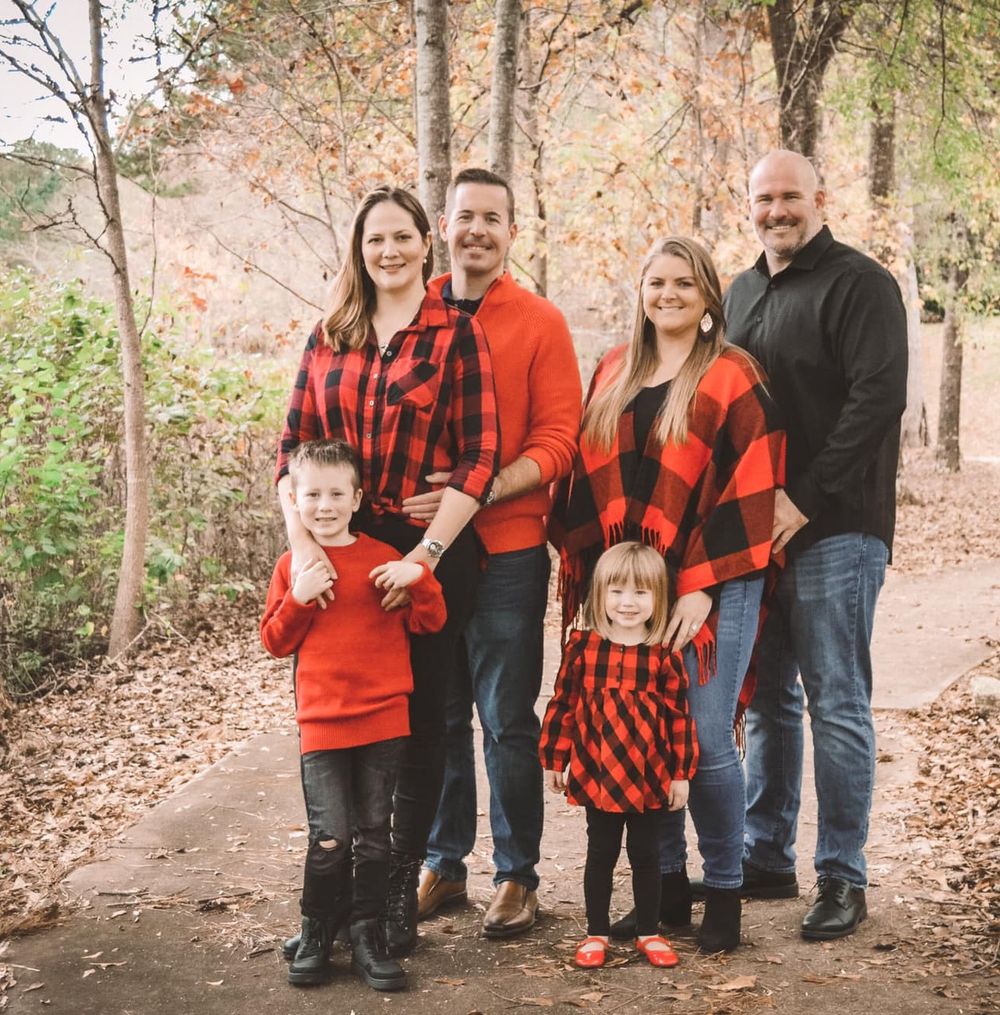 Family group wearing coordinated red and black buffalo plaid poses together in autumn woods.