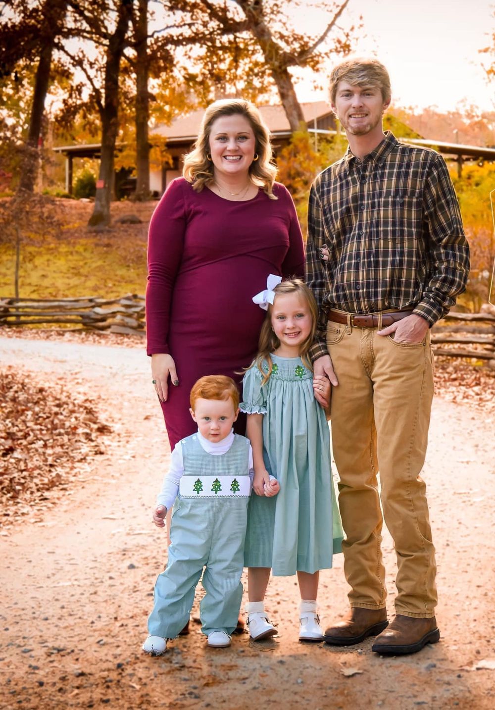 Autumn family portrait in coordinating burgundy and blue outfits standing among fallen leaves.
