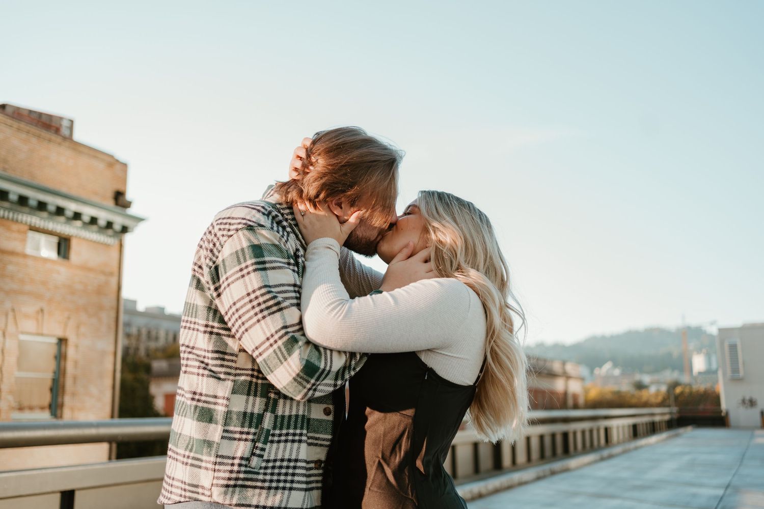 Couple sharing an intimate moment on a rooftop with city buildings in background.
