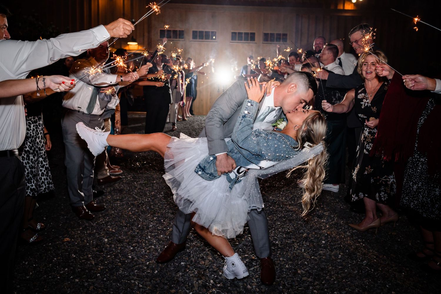 A couple dips dramatically during their sparkler exit at an evening wedding celebration.