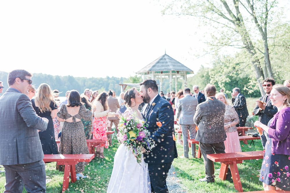Wedding guests gather outdoors around a gazebo for a springtime celebration as confetti floats through the air.