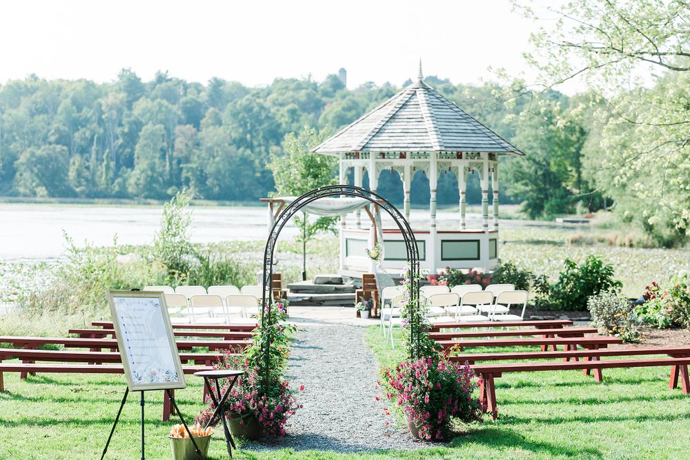White gazebo and wooden chairs set up for outdoor lakeside wedding ceremony.