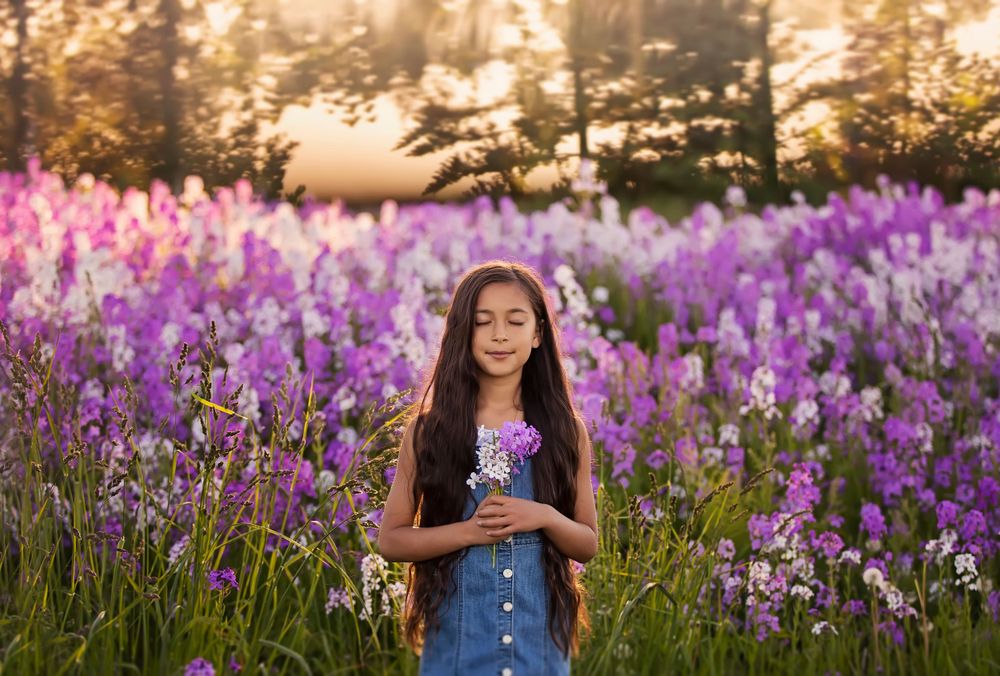Ten year old girl standing in a field of purple flowers with her eyes closed and a slight smile and beautiful, long hair