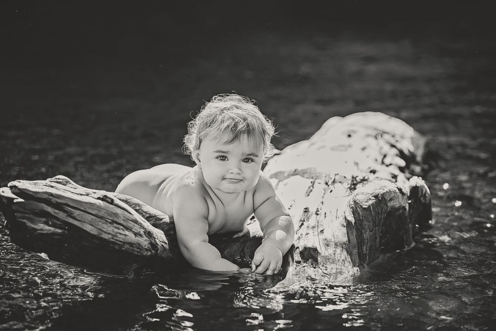 Black and white of a one year old baby with a hilarious, adorable expression relaxing on a log in Comox Lake