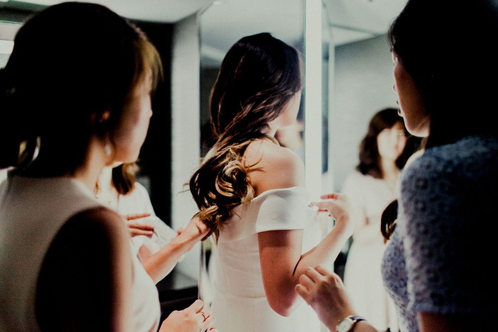 friends adjusting dress while bride getting ready