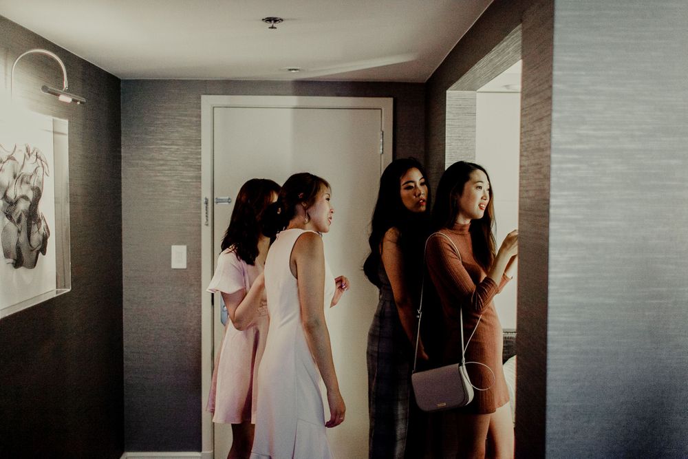 bridal party watching and helping bride prepare makeup and hair inside hotel