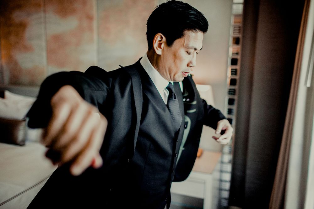groom putting on blazer in front if window