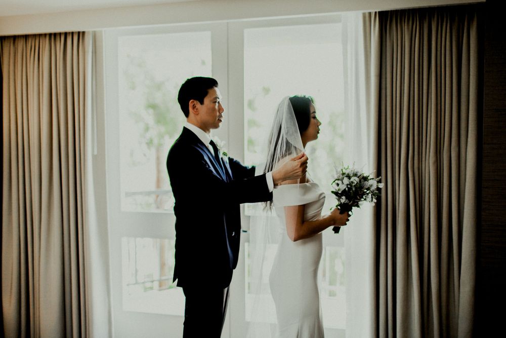 groom adjusting veil for bride in front of balcony window