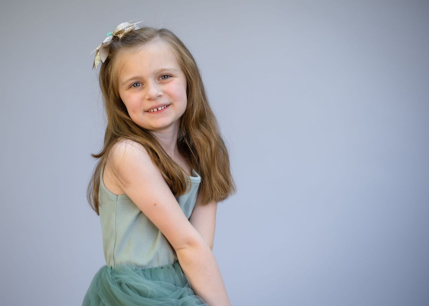 Child in mint green dress poses against gray studio backdrop.