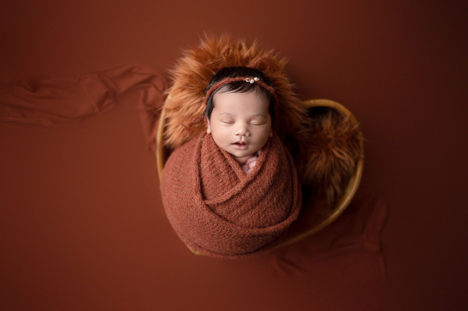 Cozy newborn photography with baby wrapped in brown knit blanket against warm backdrop.