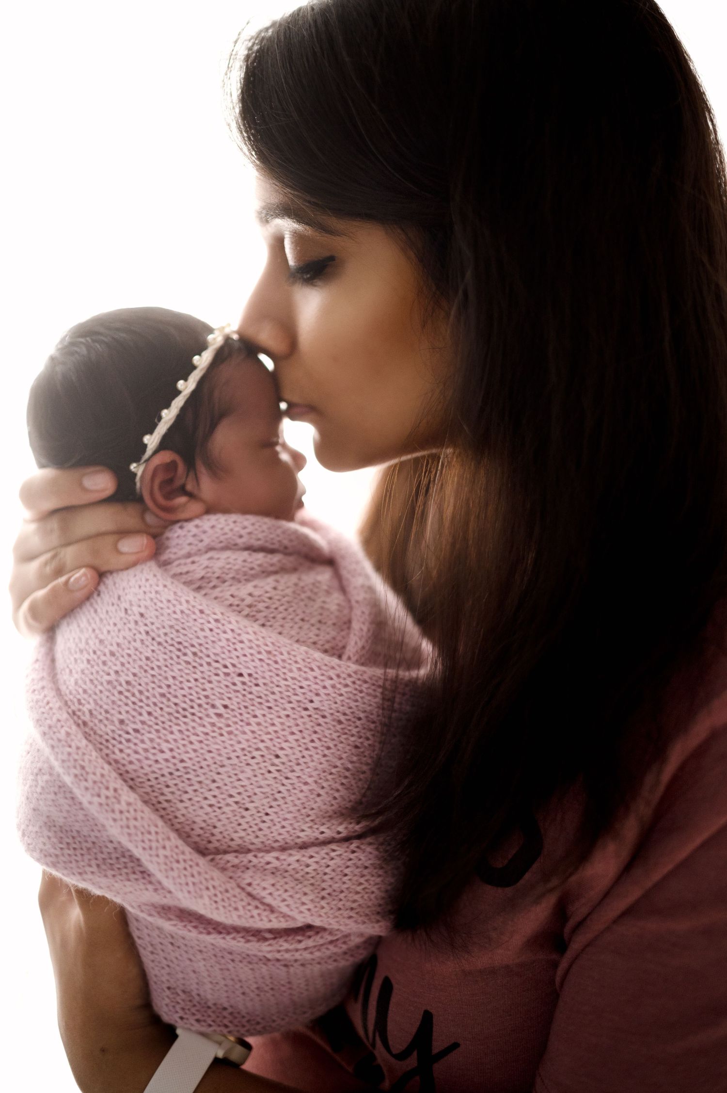 Silhouetted profile of parent holding newborn wrapped in pink knit blanket.