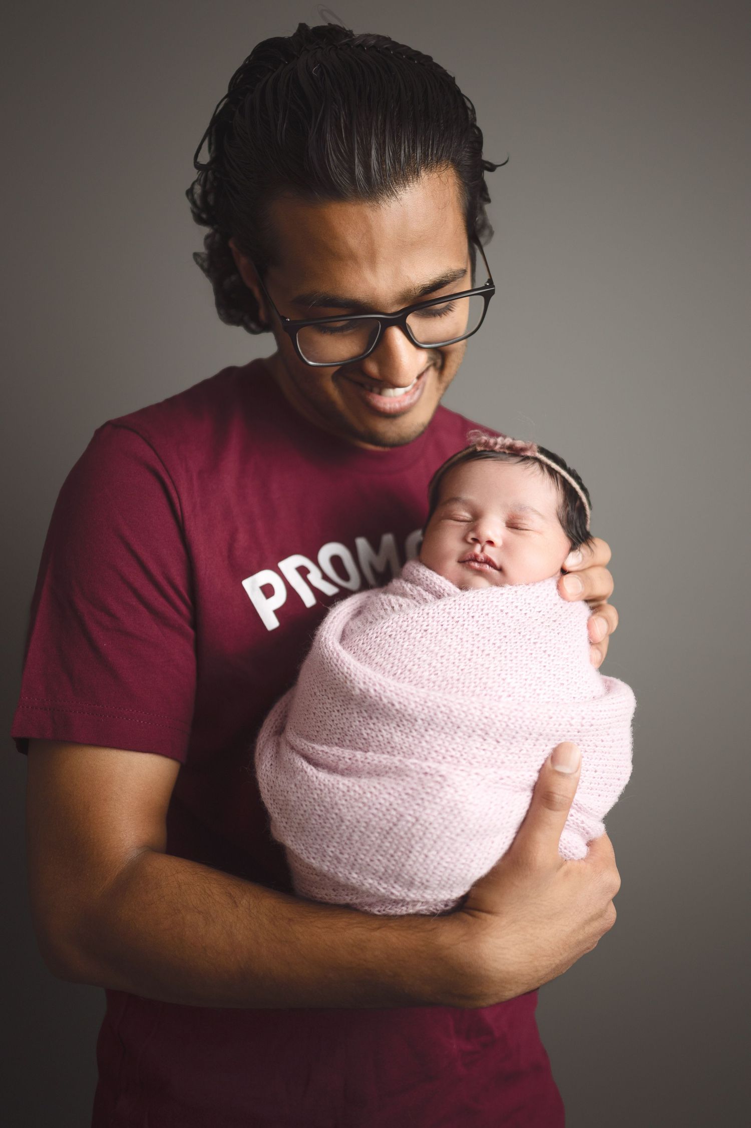 Parent giving gentle kiss to newborn baby wrapped in soft pink blanket.