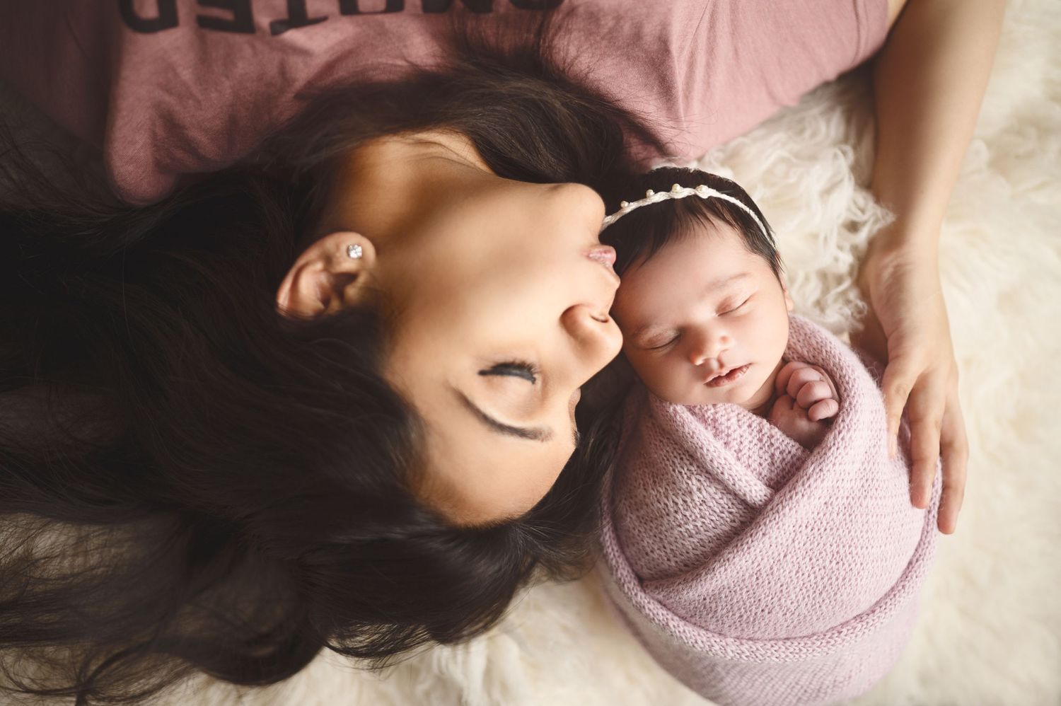 Gentle newborn portrait session showing baby wrapped in soft pink blanket against neutral backdrop.