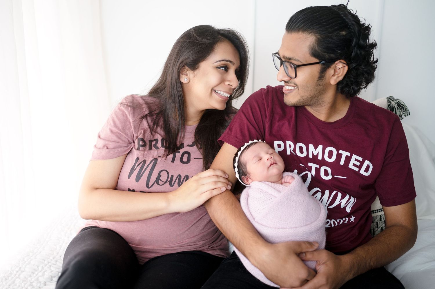 Happy parents in matching shirts share joyful moments with their newborn baby.
