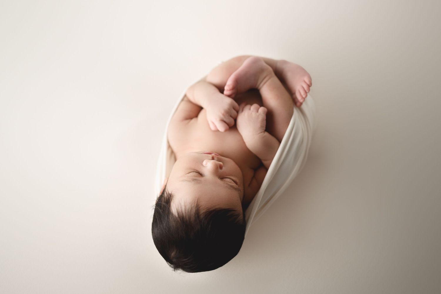 Close-up portrait of sleeping newborn with black hair on neutral background.