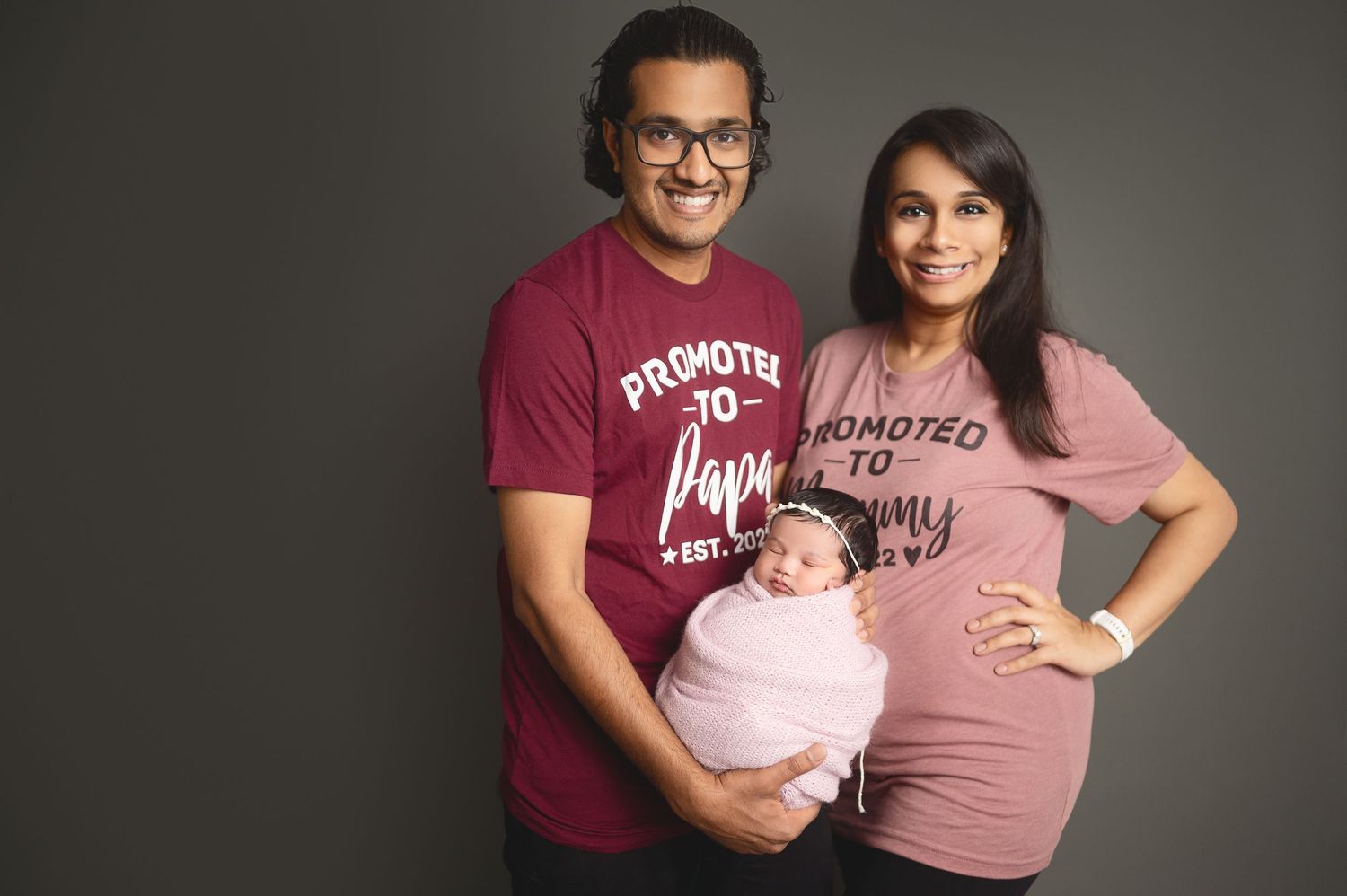 Studio family portrait session with parents in coordinating outfits holding their newborn.