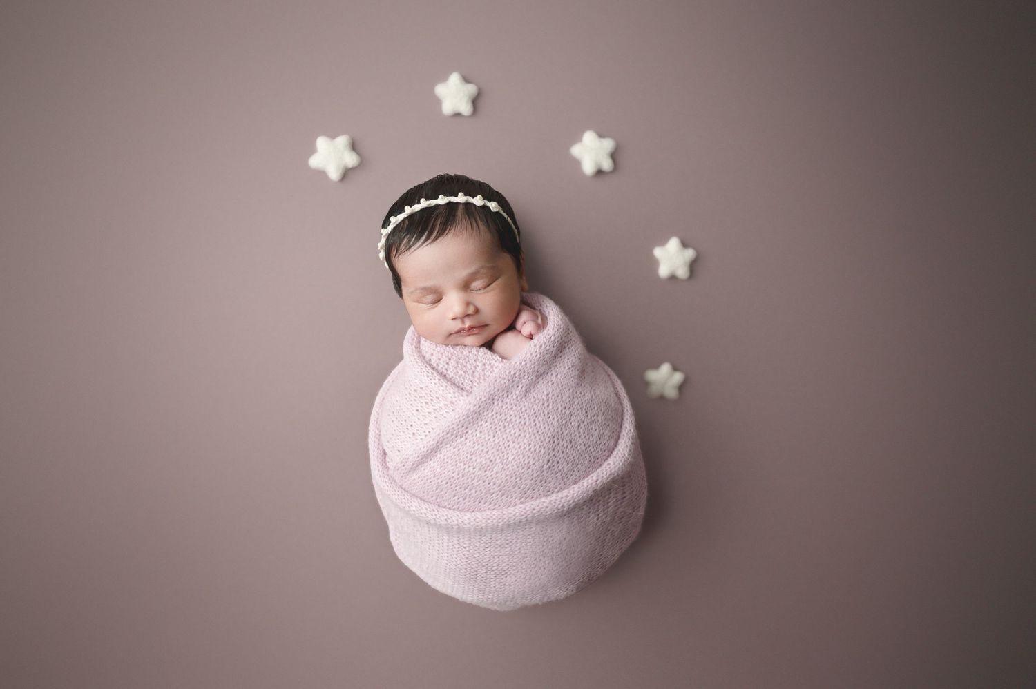 Artistic newborn photo with white star decorations and pink wrap on simple backdrop.