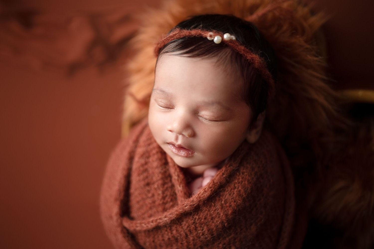 Peaceful sleeping newborn portrait with soft lighting and warm brown tones.