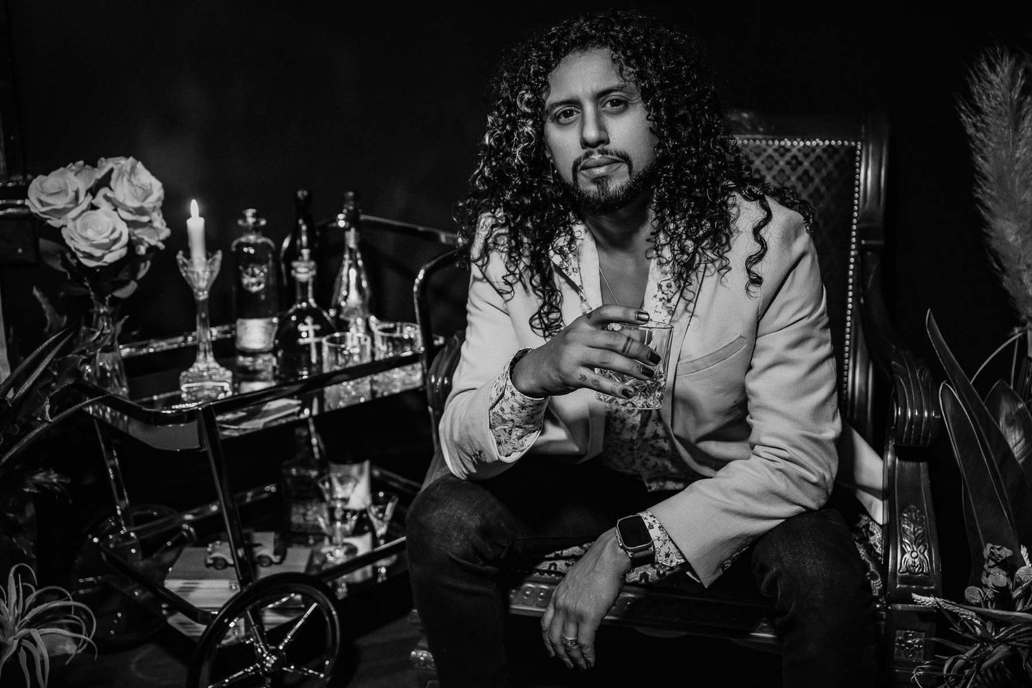Black and white photo of person sitting near bottles in moody bar setting.