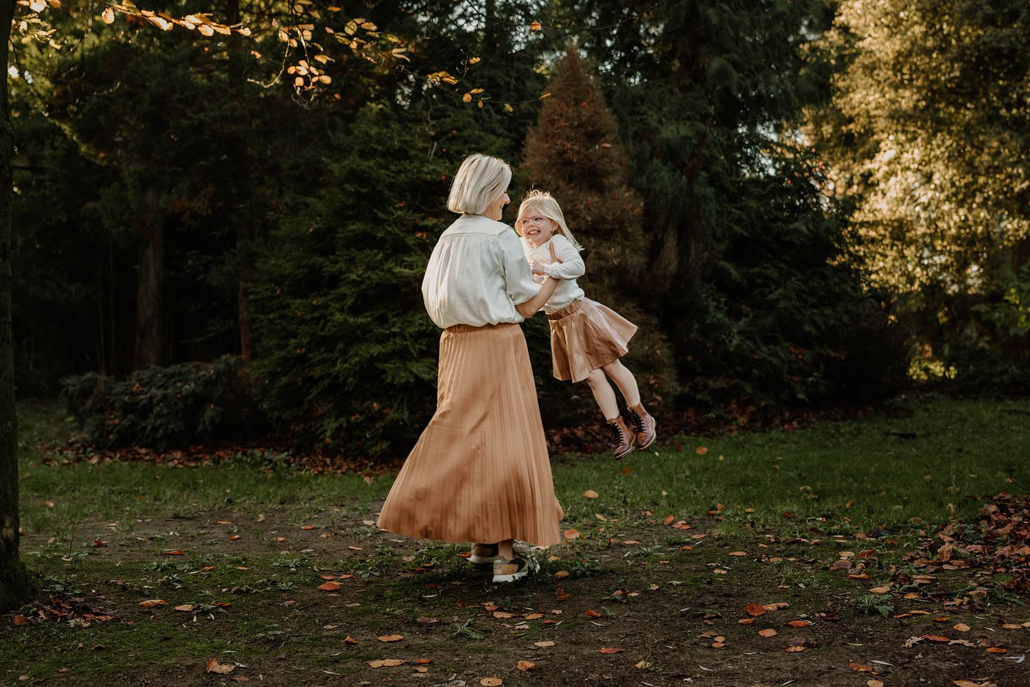 Parent and child spinning joyfully in autumn forest during golden hour.