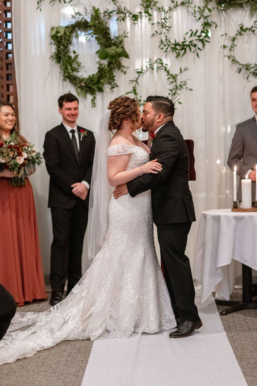 A wedding ceremony moment under greenery wreaths and white draping.