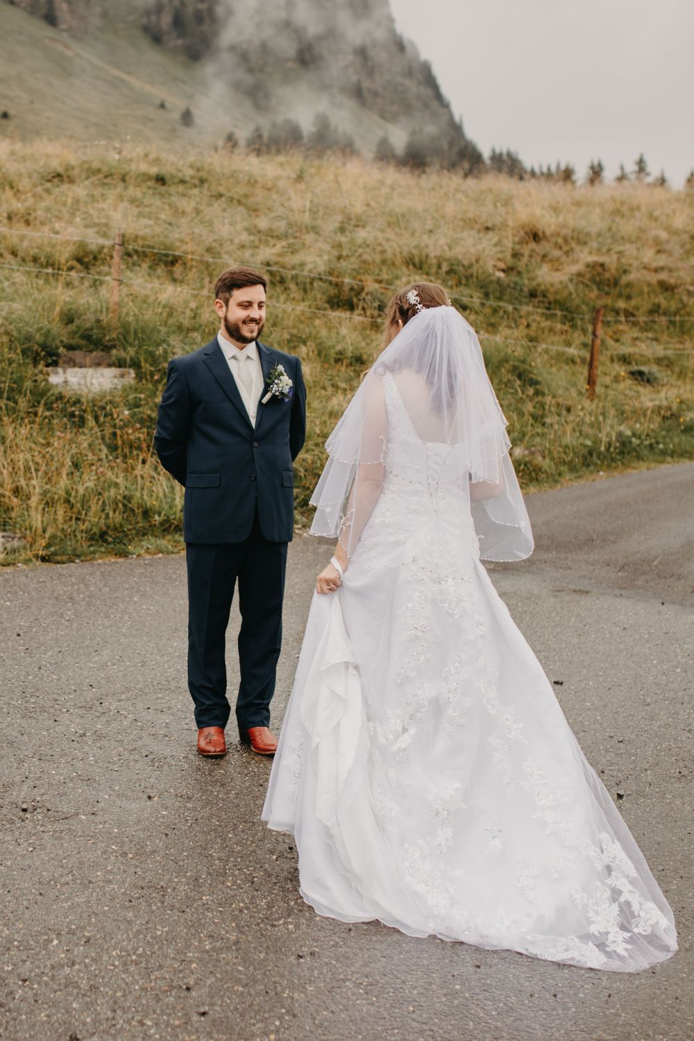 Wedding couple on mountain path with dramatic foggy peaks in background.
