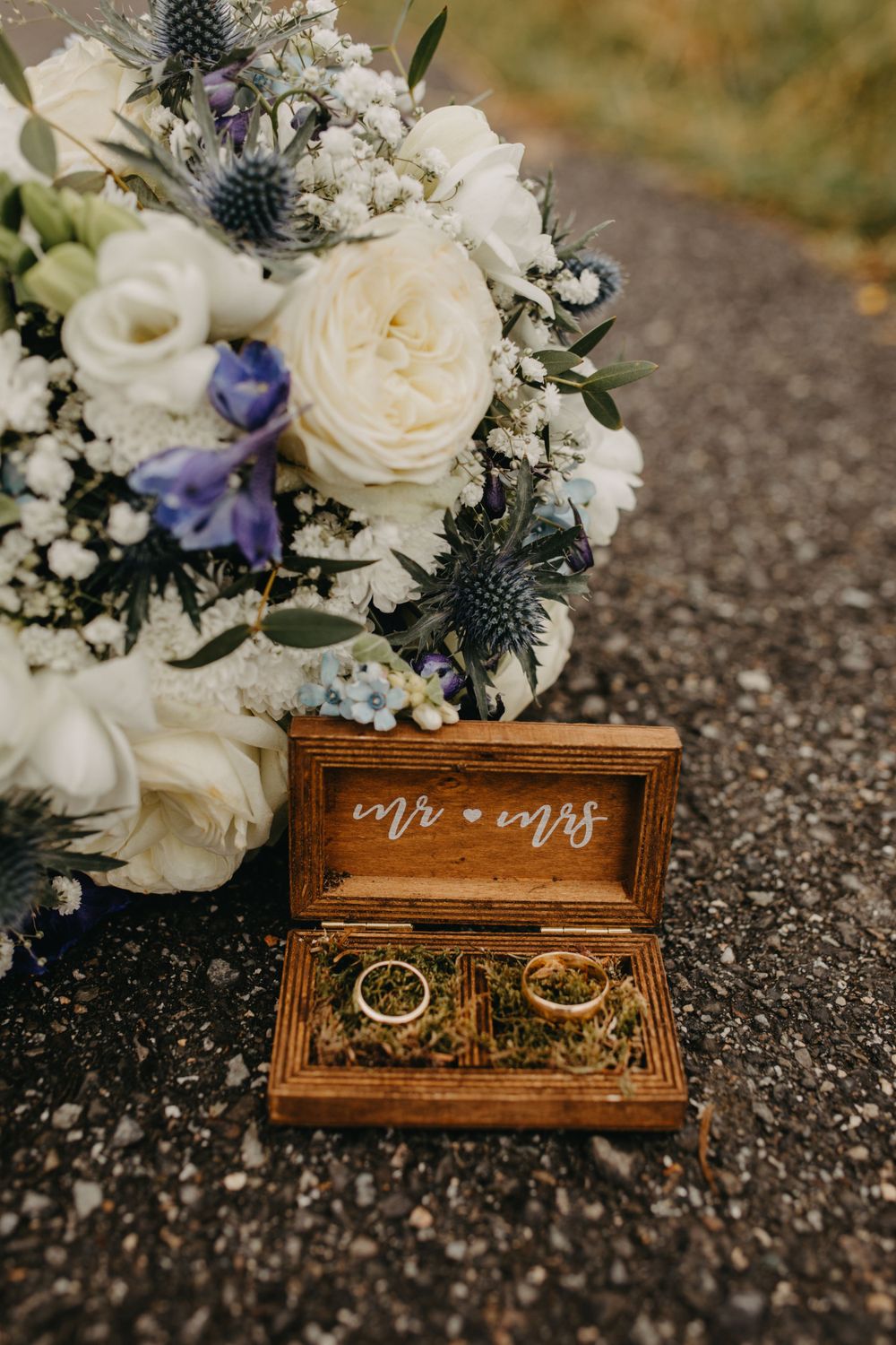 Wooden ring box with Mr & Mrs text beside elegant white and purple wedding bouquet.
