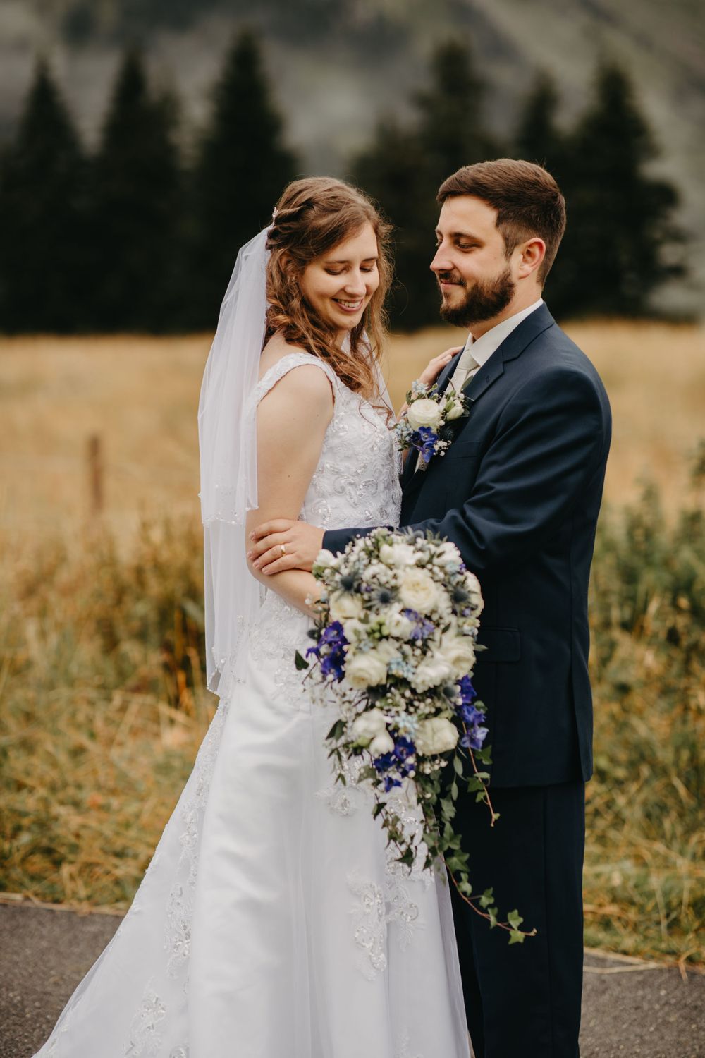 Romantic wedding portrait with beautiful bouquet of white and purple flowers against mountain backdrop.