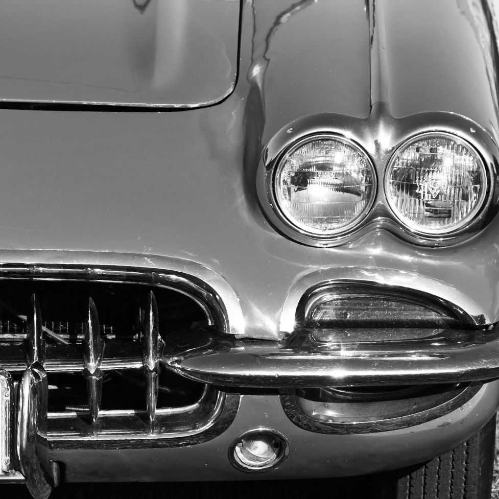 Close-up detail of classic Corvette headlights and chrome grille in monochrome.