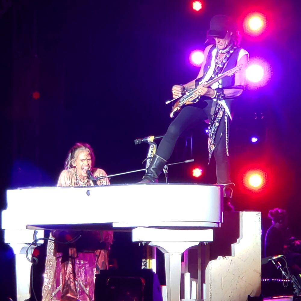 Concert performance featuring musicians with a white piano under dramatic purple lighting.