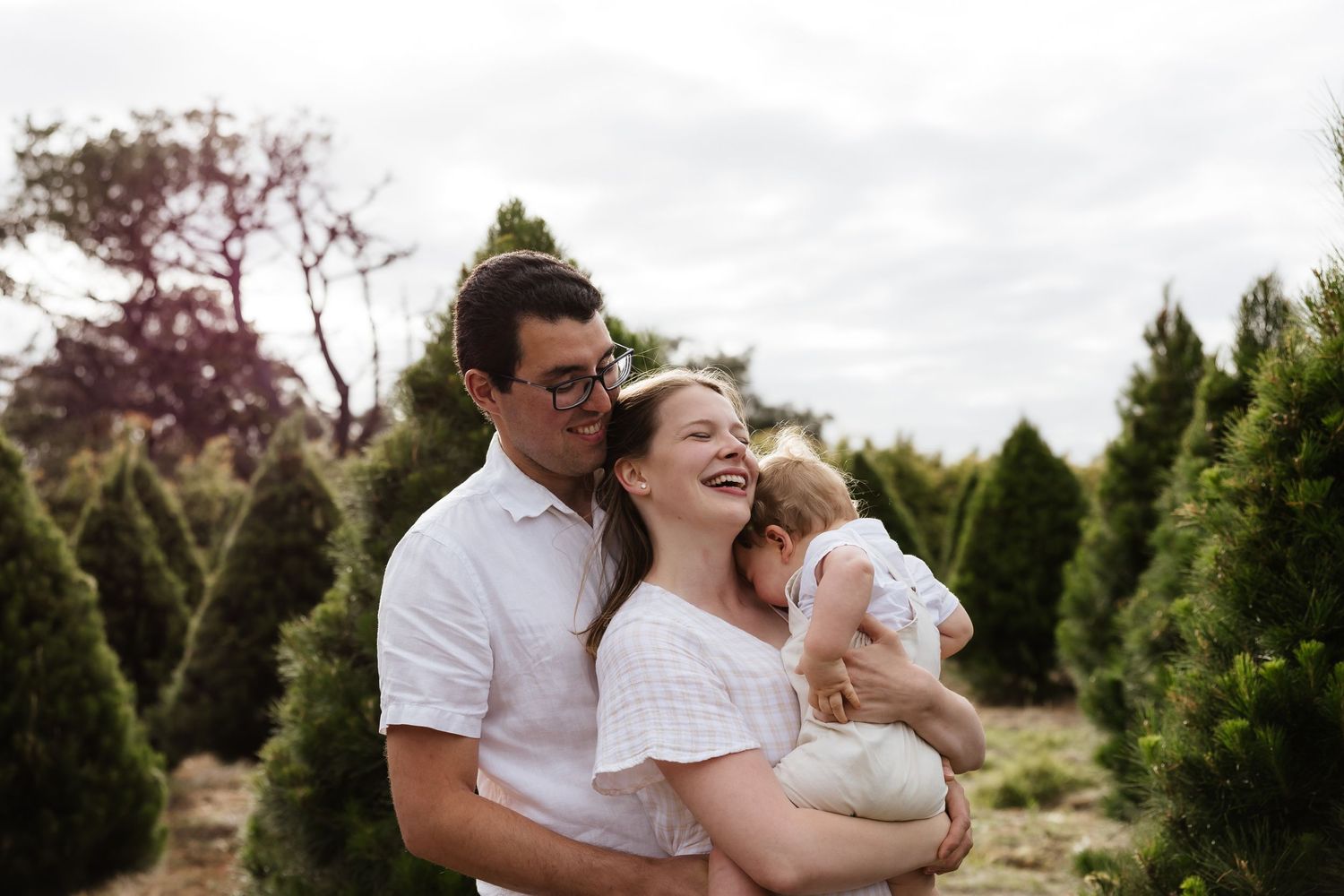 A joyful outdoor family moment among evergreen trees on a cloudy day.