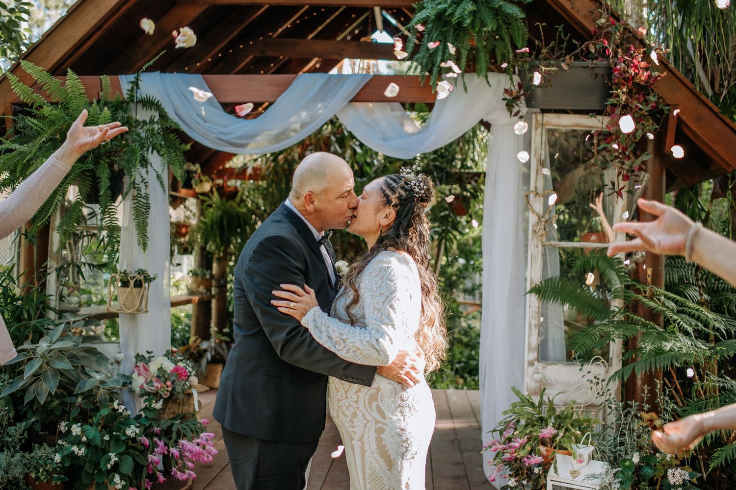 A romantic wedding kiss under an arch decorated with blue drapery and flowers.