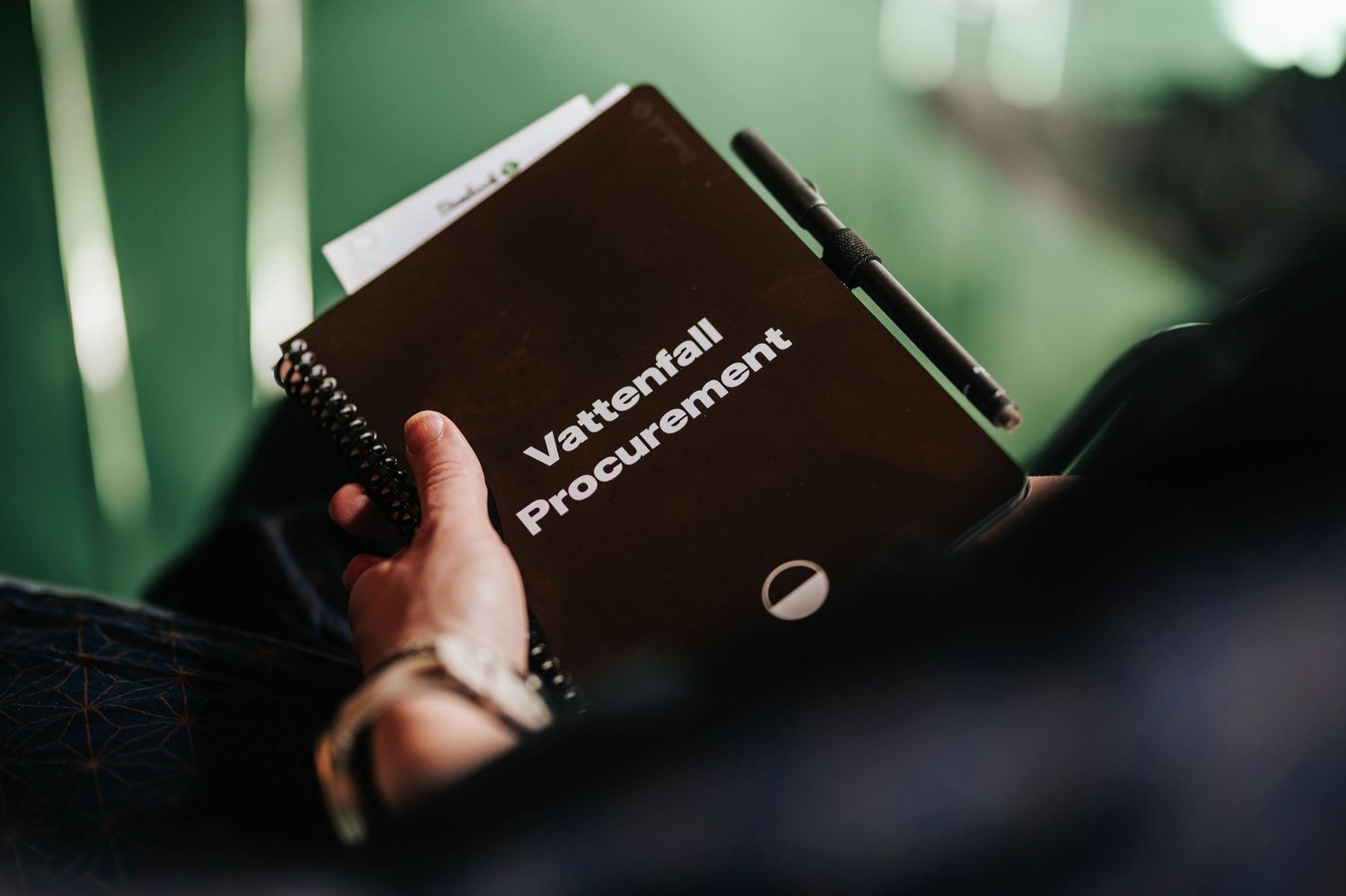 Närbild av händer som håller en svart anteckningsbok eller programguide. Vattenfall Sverige, Yasuragi