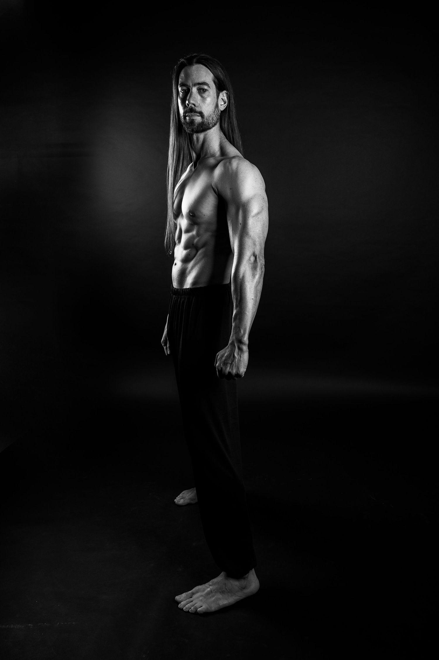Athletic figure in black pants showing muscular physique in dramatic side profile.