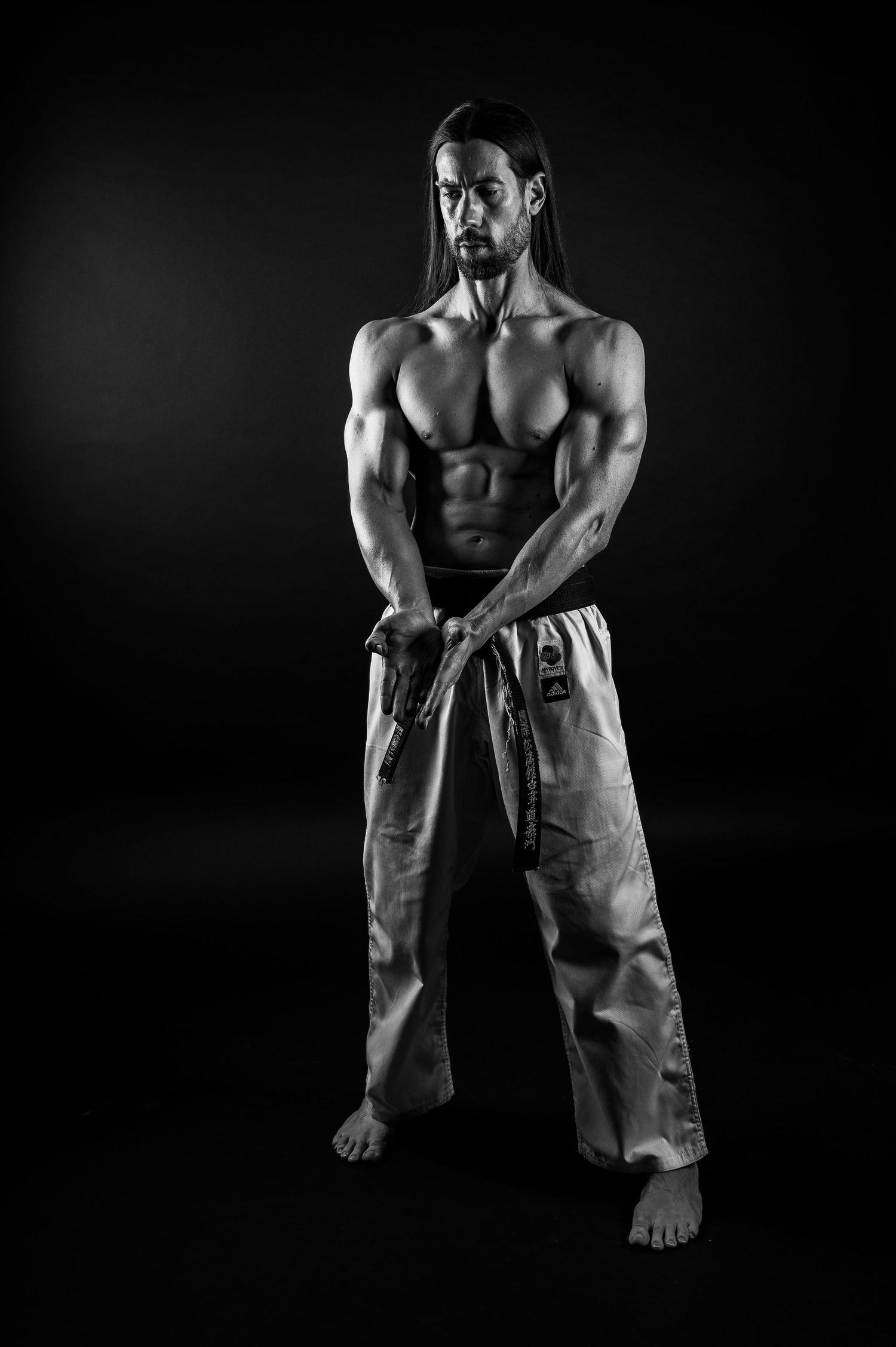 Martial arts practitioner in traditional gi pants poses in dramatic monochrome lighting.