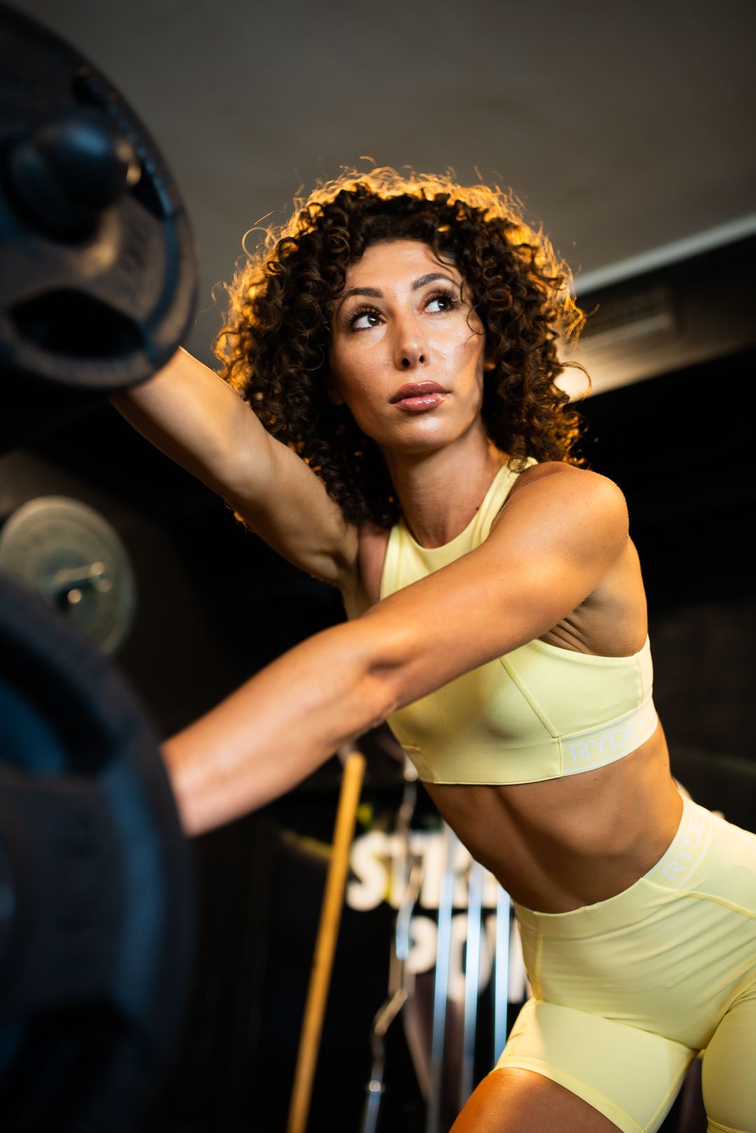 Fitness enthusiast in pale yellow workout set lifting weights during gym training session.