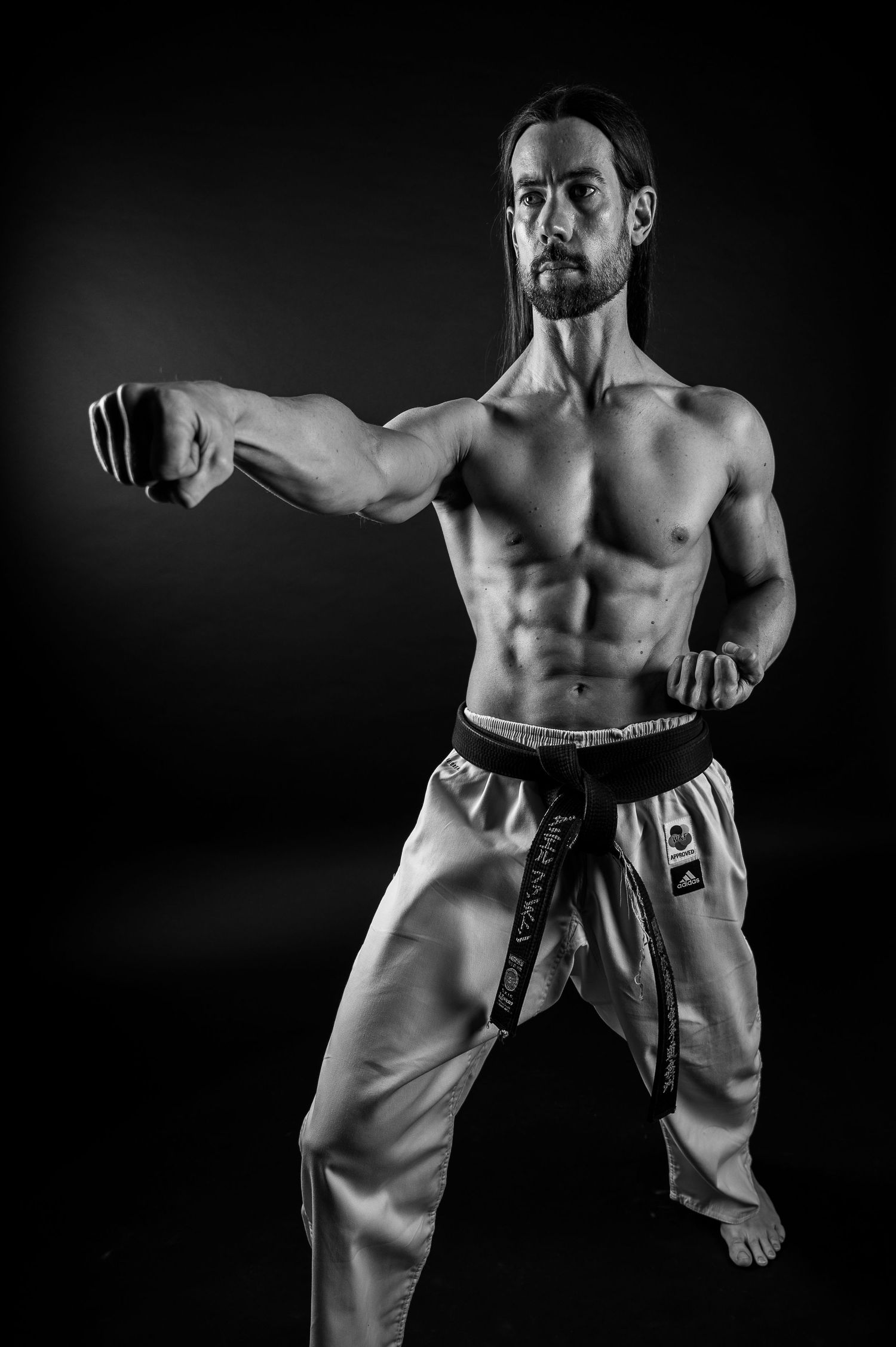 Athletic martial artist performs stance in black and white dramatic lighting.