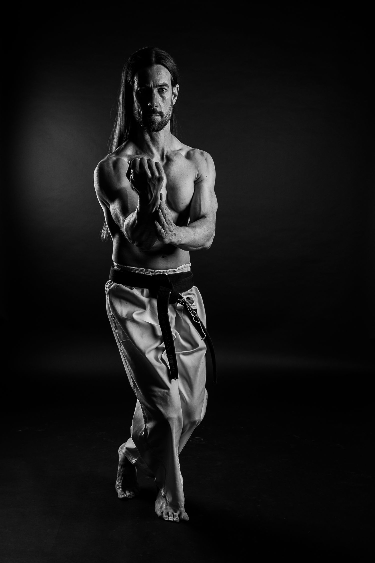 Athletic martial artist in monochrome striking powerful stance against dark background.