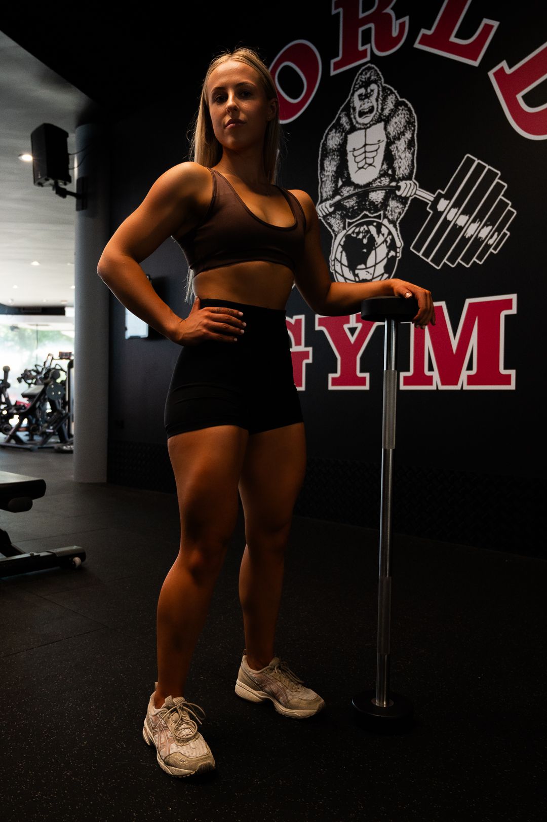 Fitness photo taken at World Gym showing athletic pose with logo wall backdrop.