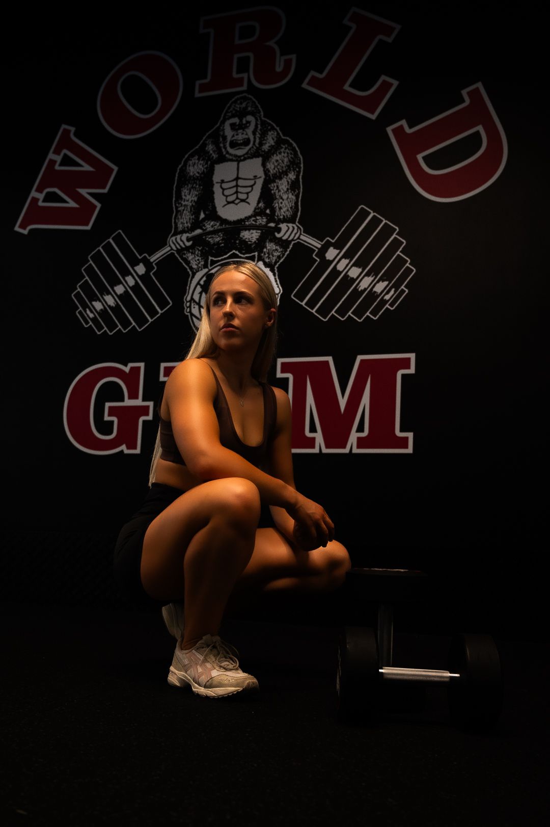 Dramatic low-light gym portrait with World Gym logo and weightlifter graphic visible.